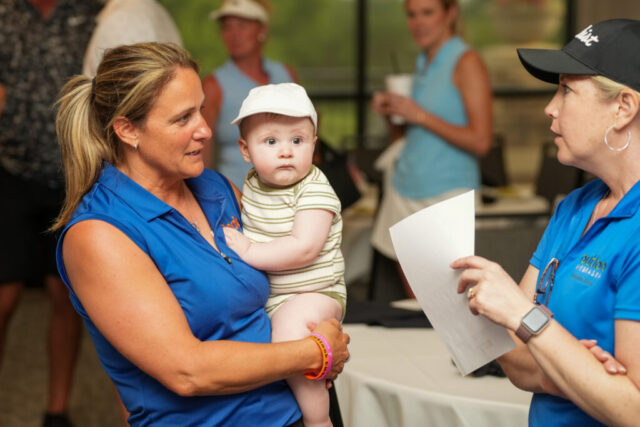 Nina is holding a baby and talking to Shilo.