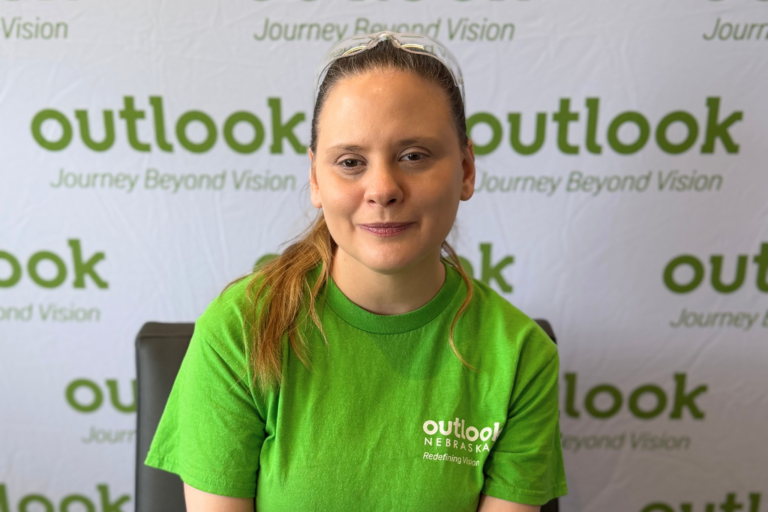 Jessica is seated and smiling in front of an "Outlook - Journey Beyond Vision" backdrop.
