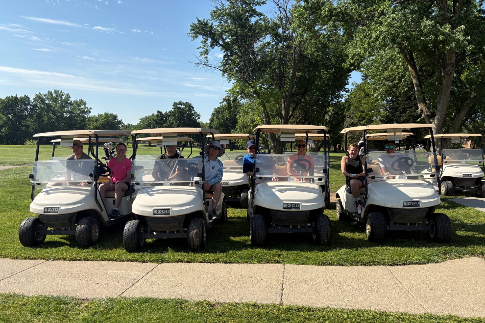 four golf carts lined up side by side with both a sighted caddy and visually impaired golfer riding in each cart.
