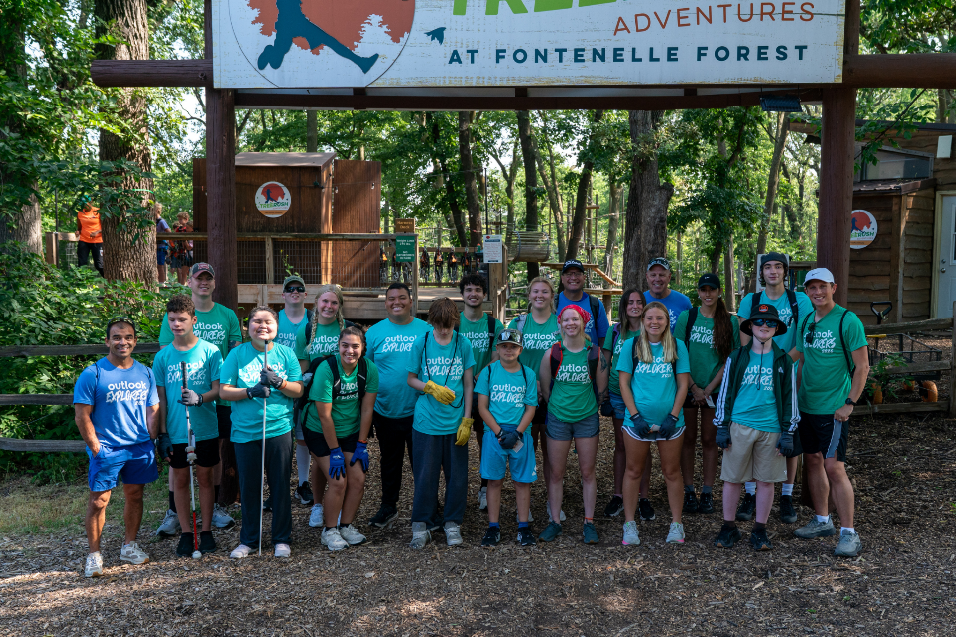 Campers and volunteers are smiling in front of the TreeRush Adventures sign.