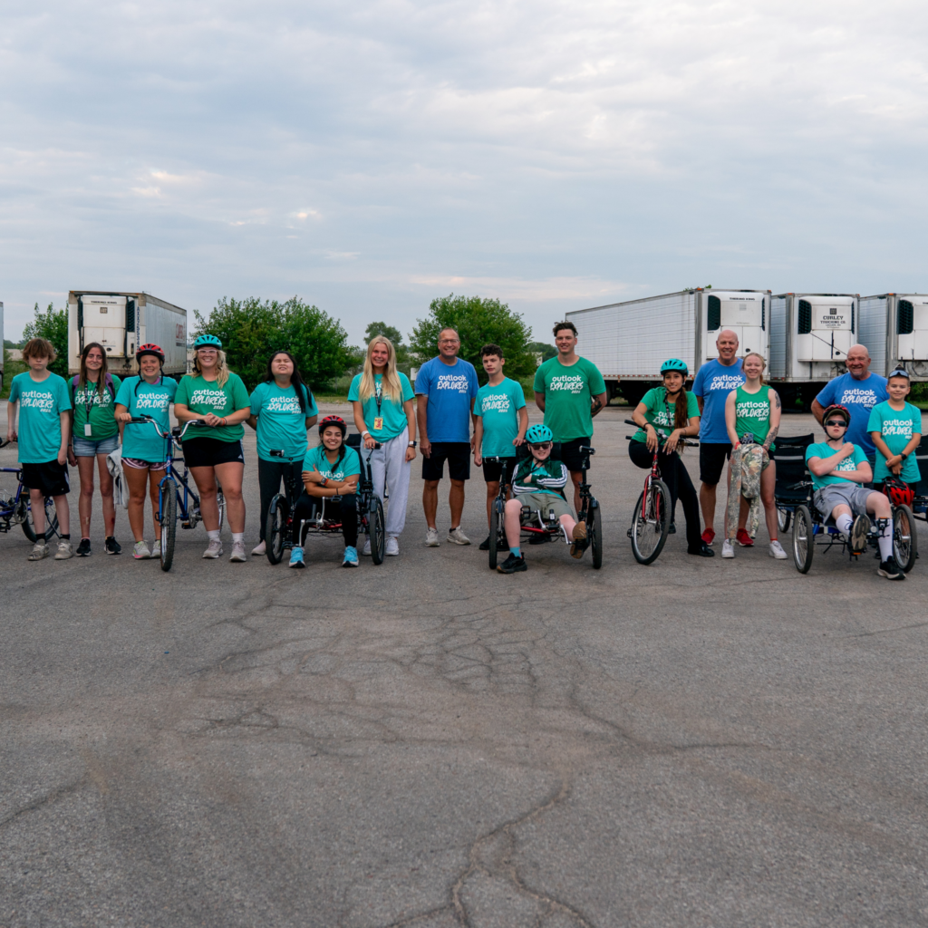 Campers and counselors are all together, smiling, either seated or beside their tandem bike.