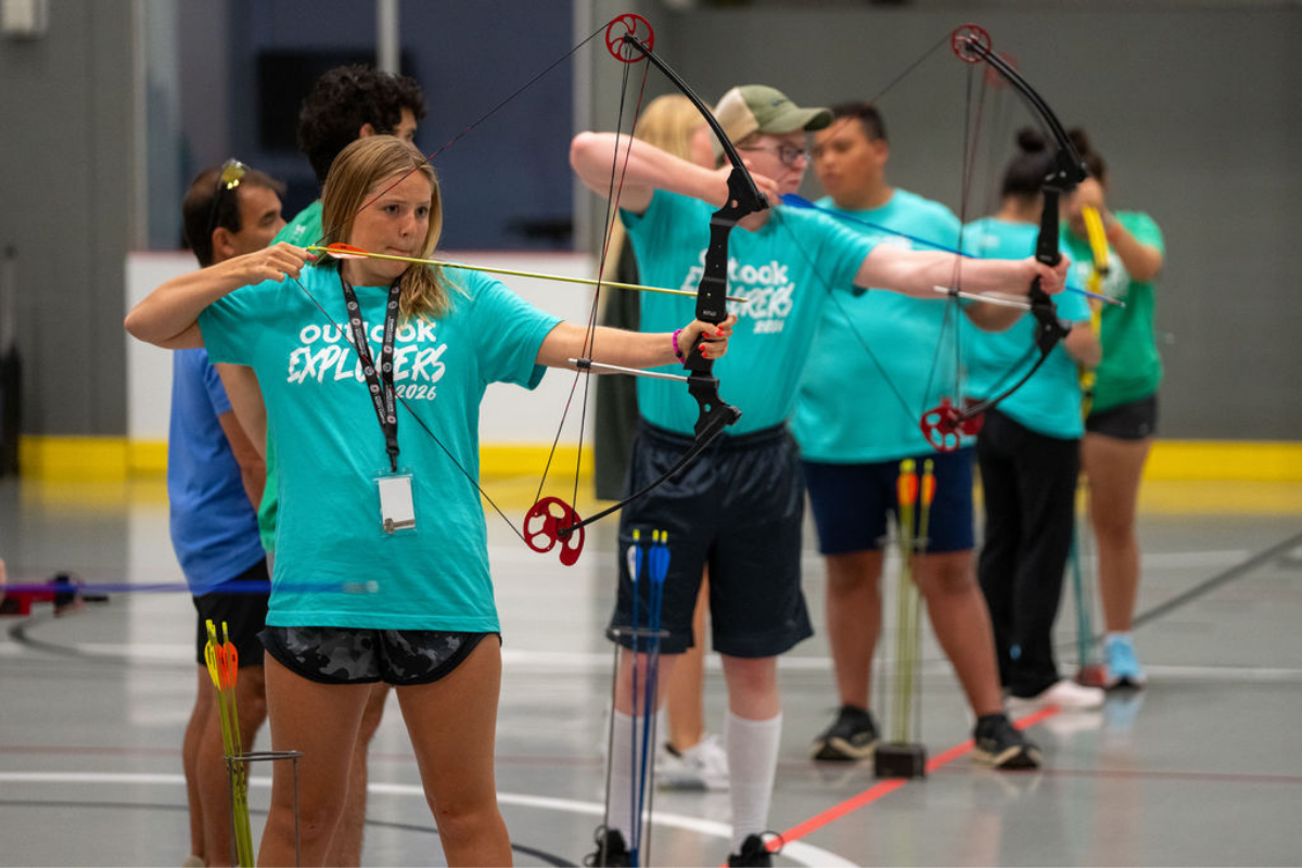 Anna is holding a bow and arrow as she practices archery.