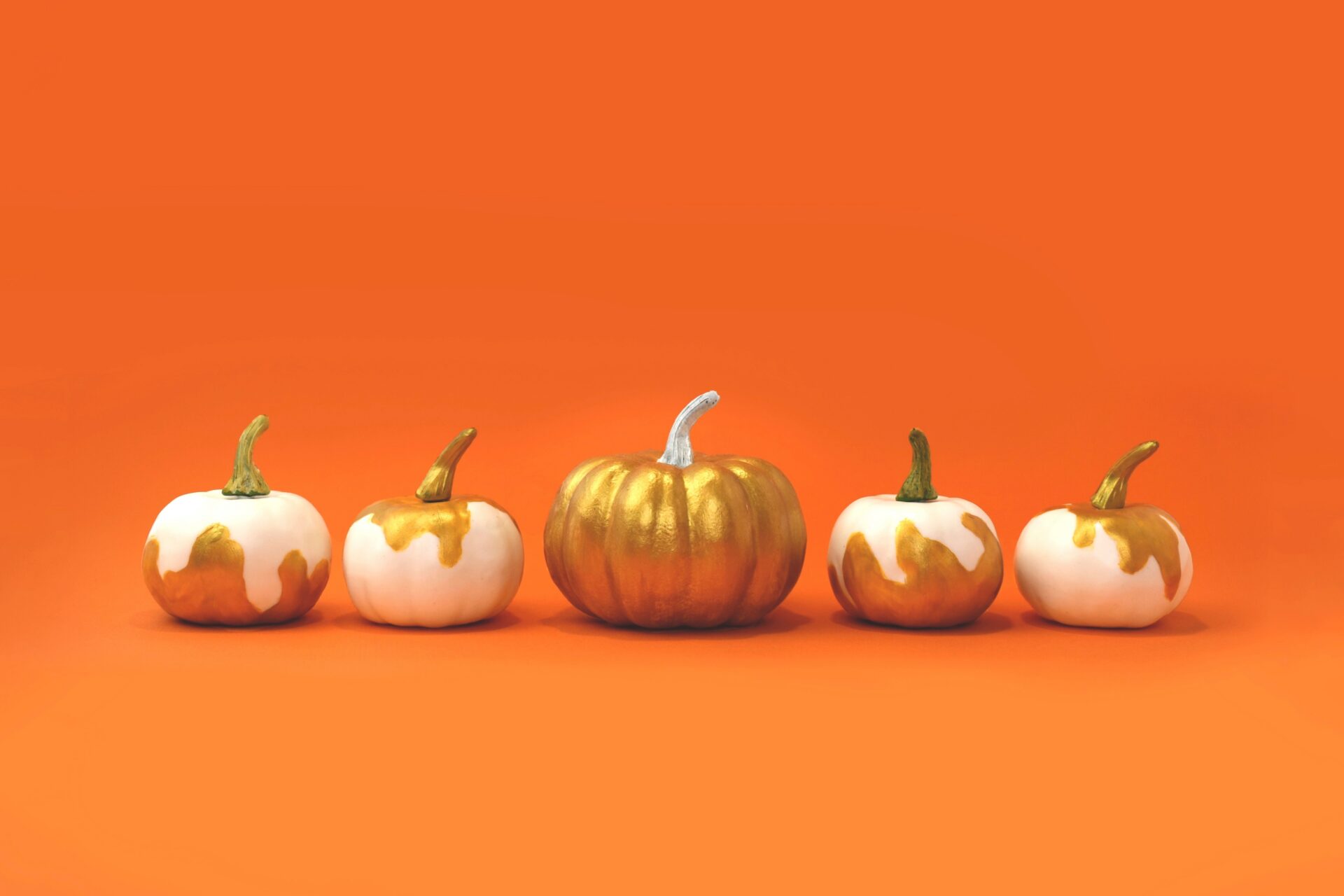 A line of orange pumpkins splattered and dropping with white paint on an orange background.
